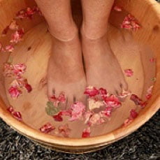 A person's feet soaking in a wooden foot bath filled with water and rose petals